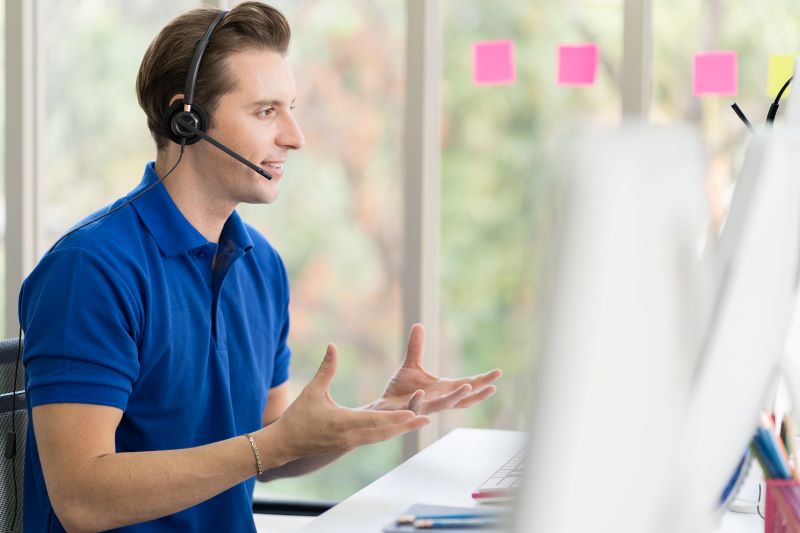Homem de headset e camiseta azul conversa online com o cliente adotando boas estratégias de comunicação.