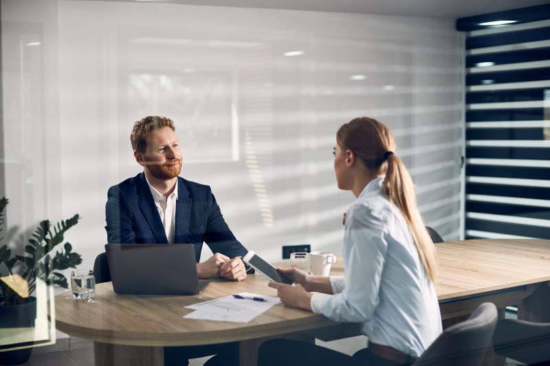 Homem conversa com uma mulher, sentados à mesa de reunião, sobre questões relacionadas à gestão contábil.