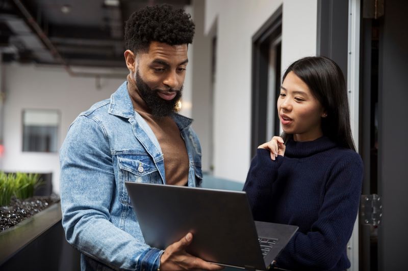 negócios que faltam no Brasil​: mulher e homem em pé com notebook conversando em corredor de empresa